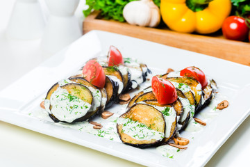 Grilled slices of eggplant and tomatoes in stack with spicy sauce