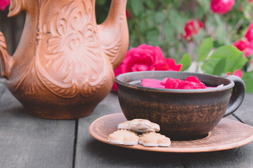 on a saucer a cup of tea of red rose petals on a wooden background.