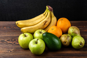 Banana, orange, avocado, pear and green apple on dark wooden background.