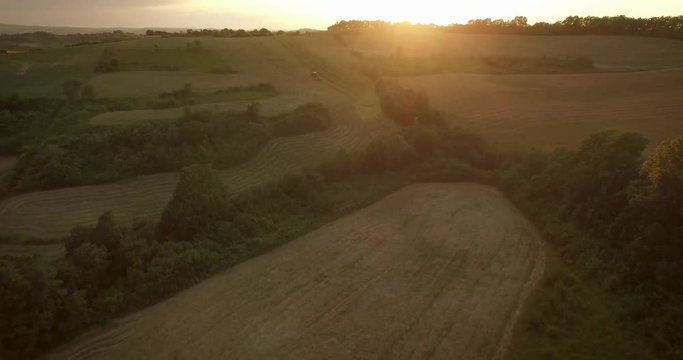 Drone flying over fields on a sunset. Following a tractor in the field