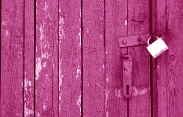 Old padlock on wooden gate in pink tone.