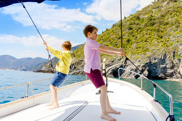 Two adorable school kid boys, best friends enjoying sailing boat trip. Family vacations on sea on sunny day. Children smiling. Brothers, schoolchilden, siblings, best friends having fun on yacht.