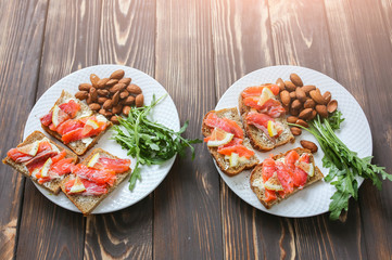 Wholemeal bread with salmon on white plate. Arugula and almond with lemon. Healthy sandwiches. Omega-3 for snack. Proper nutrition. Sport food.