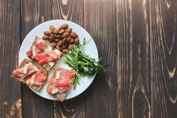 Wholemeal bread with salmon on white plate. Arugula and almond with lemon. Healthy sandwiches. Omega-3 for snack. Proper nutrition. Sport food.
