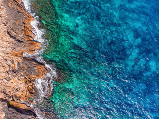 Azure clear water hits the rocky coast of coral beach. Aerial top view