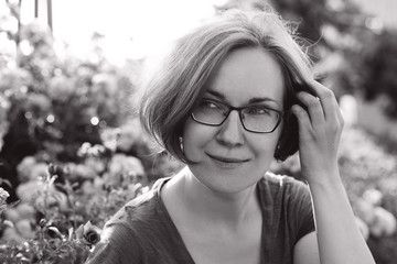 girl in glasses rests near flowers, soft sunny background