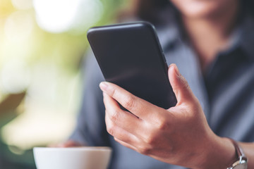 Closeup image of a woman holding  and using mobile phone with coffee cup on wooden table in cafe