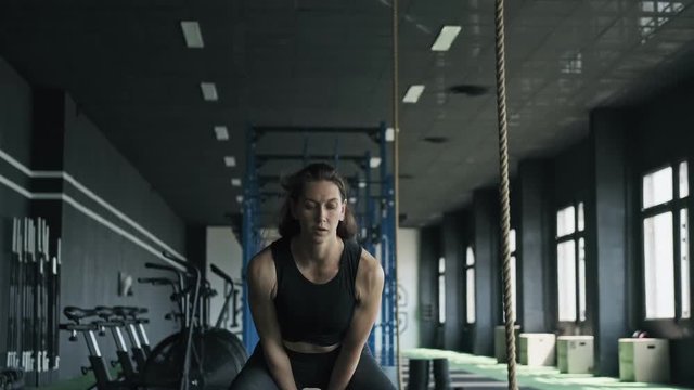 Fitness woman doing kettlebell exercise during crossfit workout at gym in slow motion. Medium shot of strong woman in black sportswear lifting up kettlebell