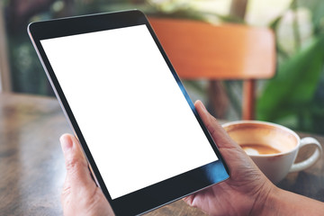 Mockup image of a woman holding black tablet pc with blank white screen with coffee cup on wooden table