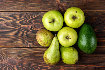 Avocado, pear and green apple on dark wooden background.