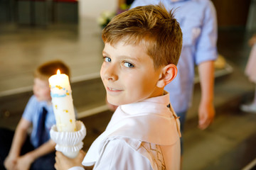 Little kid boy receiving his first holy communion. Happy child holding Christening candle....