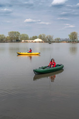 Fototapeta na wymiar Kayak fishing at lake. Two fisherwomen on inflatable boats with fishing tackle.