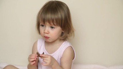 Portrait of little cute blonde child girl bites off with big appetite piece of tasty milky chocolate, eats and smiles