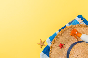 Beach flat lay accessories with copy space. Striped blue and white towel, seashells, staw sunhat and a bottle of sunblock on yellow background. Summer holiday concept