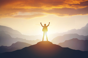 Man standing on edge of mountain feeling victorious with arms up in the air.