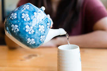 Close up young asian woman pouring hot green tea in to the tea cup in Japanese restaurant.