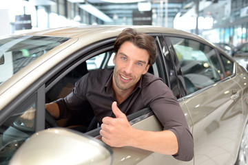 Car dealership - young handsome man sits in a car and  buying a car