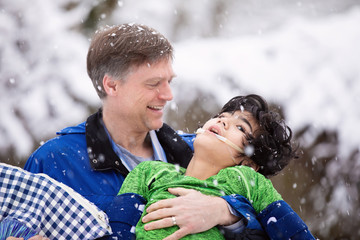 Father holding disabled son outdoors while enjoying snowfall