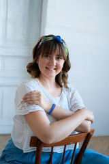 A young plus size woman sits on a chair in a spacious white room. Smile on his face, flirtatious look. Happiness and beauty in any weight. A girl in a long skirt, sandals with high heels