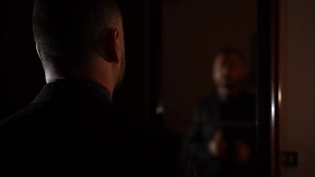 slow motion clip taken from behind of a man wearing a black suit and looking into a mirror