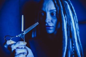 girl hairdresser with dreadlocks holding scissors in hand close-up