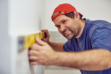 Worker using bubble level for walls and tiles inside the house - renovation fixes.