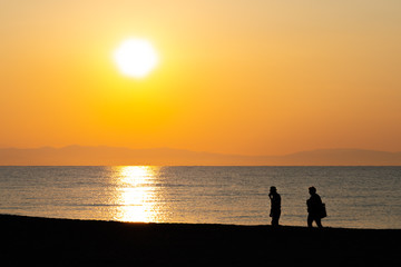 Naklejka na ściany i meble Silhouette of an elderly couple walking on the beach in sunrise / sunset on their vacation