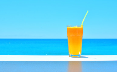Orange fresh juice in a glass on the table with blue sea backdrop. Copy space.