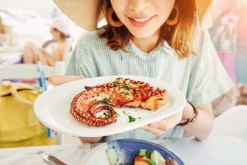 Happy asian woman in hat eating delicious grilled octopus in seafood restaurant. Delicacy and healthy gourmet cuisine © EdNurg