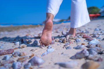 Close up low angle woman barefoot walking on beach with stone ground