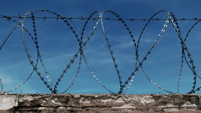 The fence of the correctional facility with barbed wire on the background of a gloomy cloudy dark blue sky.