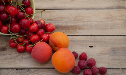 scattered berries from a plate of raspberry cherries apricots on a wooden table