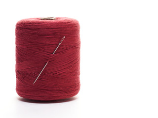 Red spool of thread with needle in a vertical position on a white background
