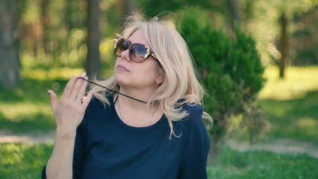 young blond woman in sunglasses in nature straightens her hair