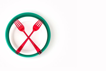 Green and white disposable plastic plates isolated on white background and crossed red forks. Ecology problem. No plastic concept. Top view. 