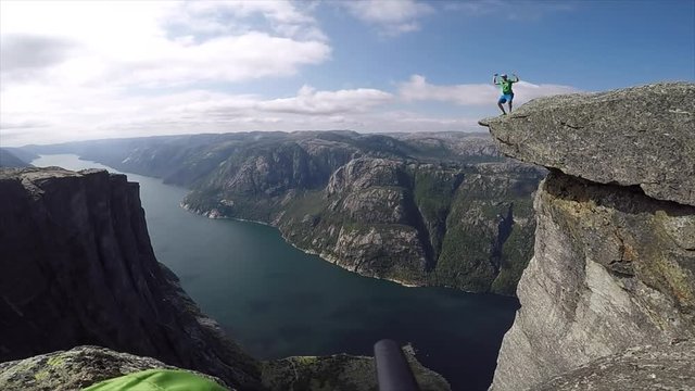 happy man jumping on the edge of high cliff with fjord on background in norway