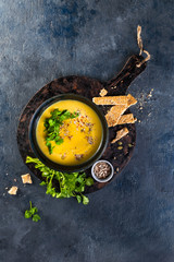 Pumpkin and vegetables cream soup with pumpkin seeds, slices of bread and parsley over a dark background with Space for text. Vegan Food Concept. Hard sunlight, hard shadows, top view.
