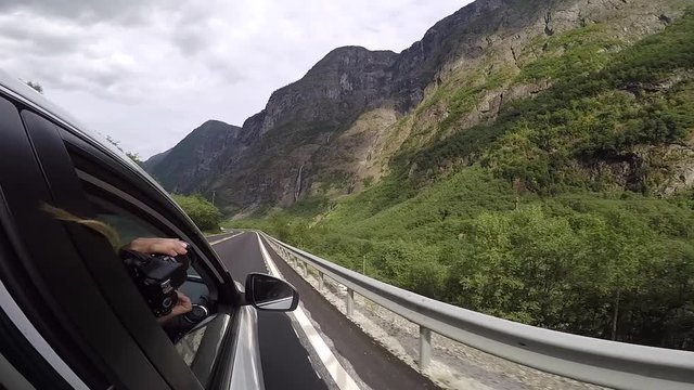 Girl passenger taking picture of mountains out of window with photo camera in beautiful Norway