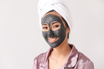 Beautiful Asian woman with facial mask on light background