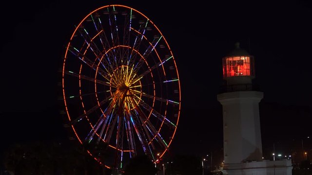 The Ferris wheel and lighthouse at night in the center of Batumi, Georgia. Night view on the illuminated ferris wheel and lighthouse on the Batumi Seafront Promenade on the coast of the Black sea.