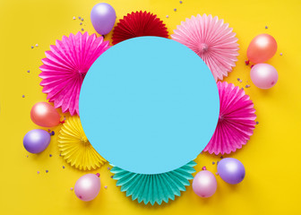 Colorful balloons and paper flowers on yellow table top view. Festive or party background. Flat lay style. Copy space for text. Birthday greeting card.
