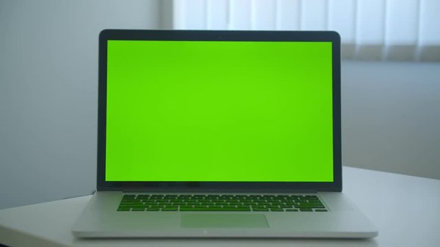 Closeup shoot of laptop with green chroma key screen laying on the table in the office indoors