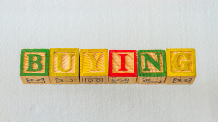 The term buying visually displayed on a clear background using colorful wooden blocks image in...