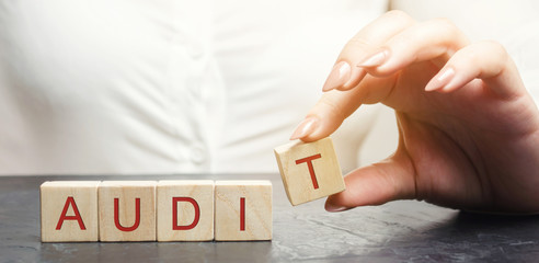 A woman puts wooden blocks with the word Audit. Inspection of financial and economic activities of...