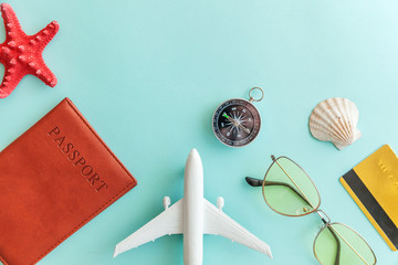 Vacation travel adventure trip concept. Minimal simple flat lay with plane passport sunglasses compass gold credit card shell on blue pastel colourful trendy background. Tourist essentials Copy space