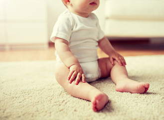 childhood, babyhood and people concept - happy little baby boy or girl sitting on floor at home