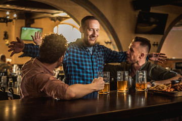 Friends drinking draft beer and watching tv in a pub
