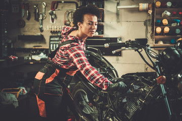 Naklejka premium African american woman mechanic repairing a motorcycle in a workshop
