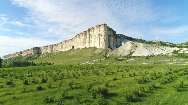 View of picturesque high white cliff near the beautiful green meadow with shrubs and other plants against blue cloudy sky in summer day. Shot. Summer landscape