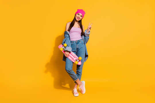 Full length body size photo beautiful she her lady amazing nice look hand arm skate board dangerous sport v-sign symbol wear casual jeans denim jacket shoes pink hat isolated yellow vivid background